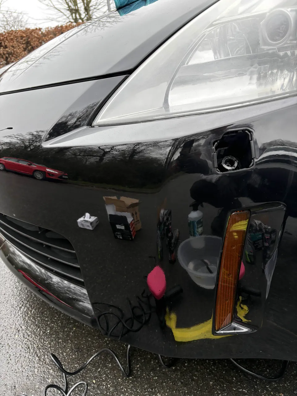 Close-up of a headlight and bonnet edge mid-correction, polish and microfibre cloths staged on the panel