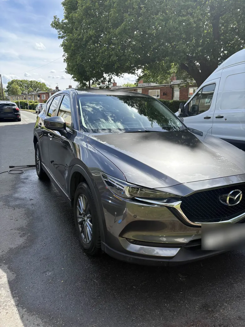 Grey Mazda CX-5 on a wet street after a wash, its paint reflecting the trees overhead, number plate blurred
